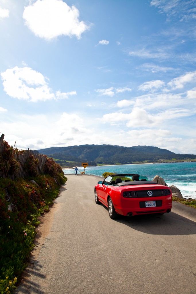 Driving along California's Pacific Coast Highway in a hot red convertible car.