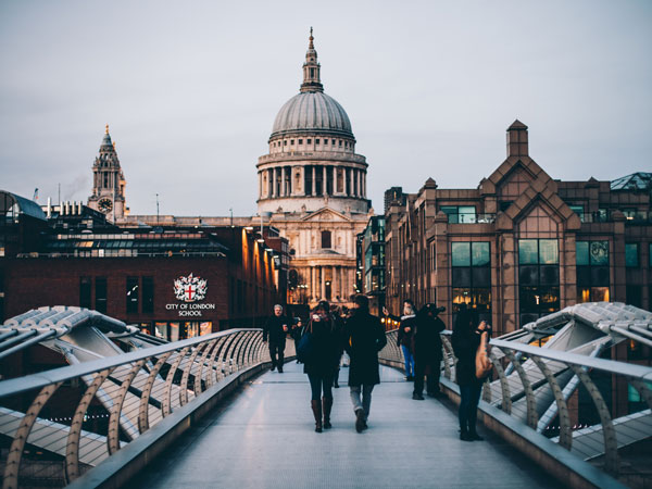 People crossing a footbridge in London with a view of the city behind them