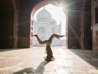 Young woman practicing yoga in India at the famous Taj Mahal at sunrise - Headstand position upside down- People travel spirituality zen like concept