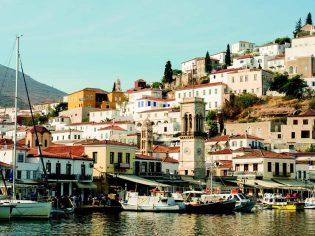Wide shot of boats on Hydra Harbour with buildings around. Greece.