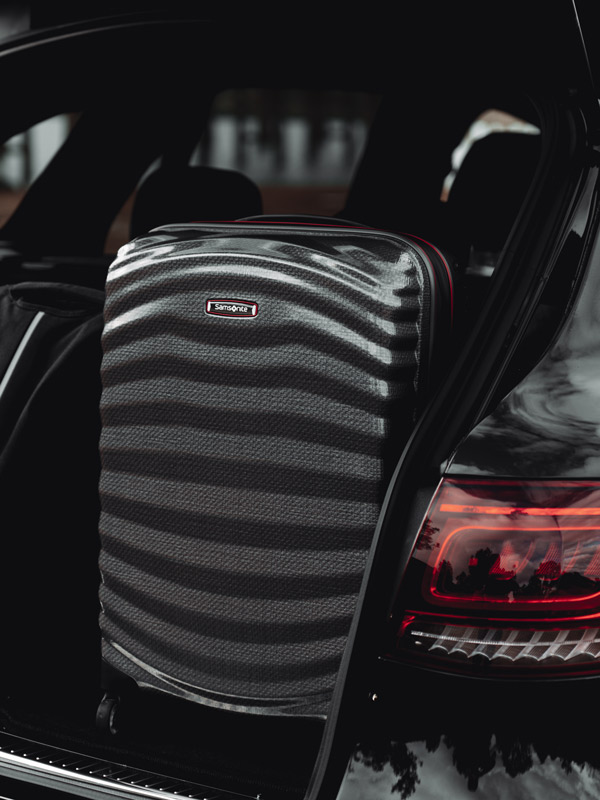 A black suitcase in the booth of a black car.