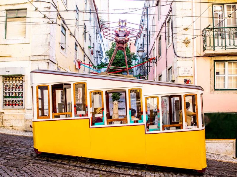 a yellow-coloured tram traversing along the Lisbon streetscape