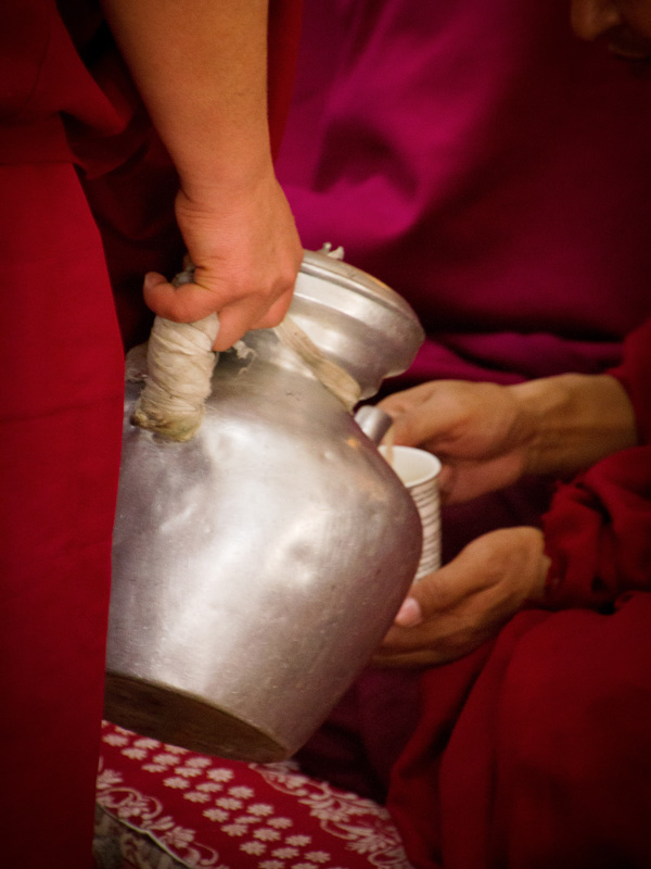 a monk holding a pitcher of Yak-butter tea and pouring it into a glass