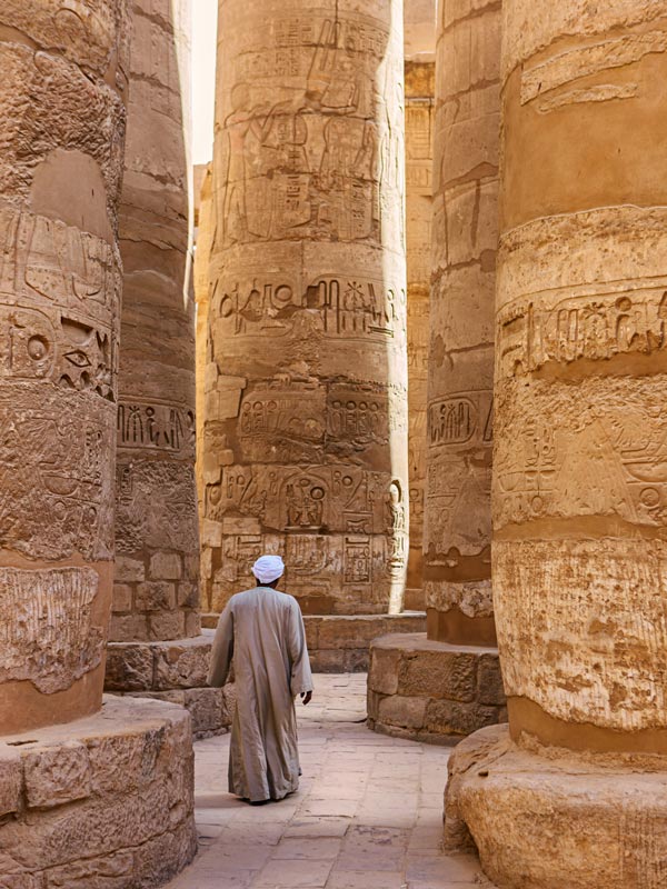 an Egyptian man walking along the colossal pillar in Karnak