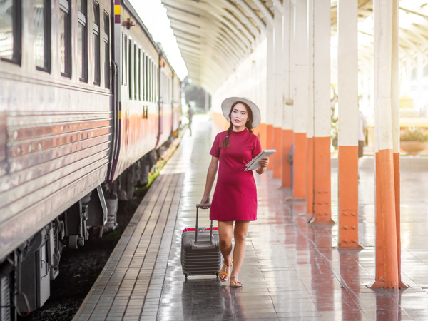 a pregnant woman in red with luggage about to ride a train