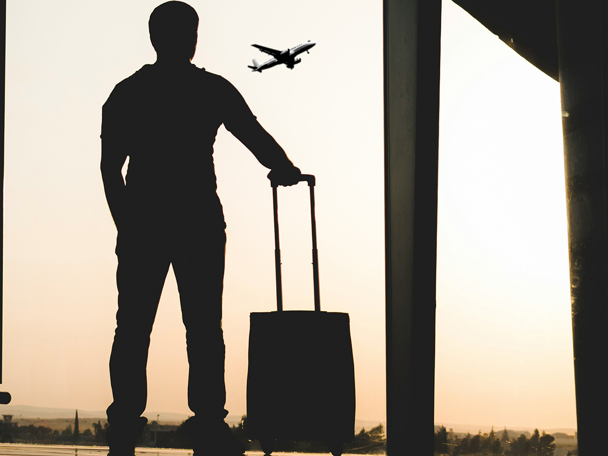 man holding luggage at airport watching plane