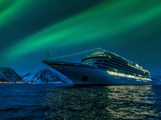 Aurora borealis above viking cruise ship in Oksfjord Norway. Green northern lights above mountains