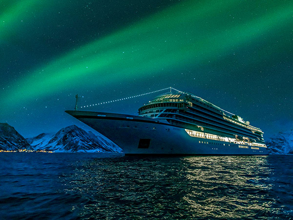 Aurora borealis above viking cruise ship in Oksfjord Norway. Green northern lights above mountains