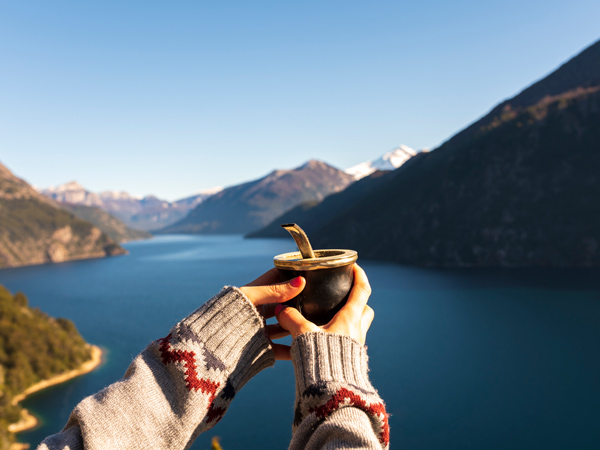 holding a cup of mate with the scenic landscape of Bariloche in the background