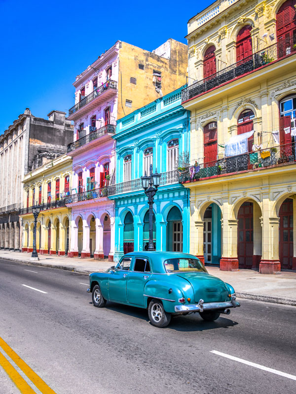 a vintage blue car nagivating a colourful street in Havana