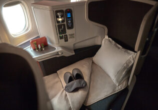 the window seat with a plush pillow, blanket, slipper and a mattress topper at Cathay Pacific Business Class
