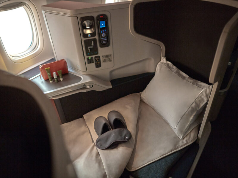 the window seat with a plush pillow, blanket, slipper and a mattress topper at Cathay Pacific Business Class