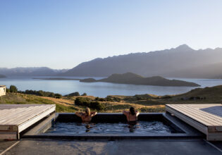 Two people relax in a tranquil pool, taking in the breathtaking alpine scenery surrounding Aro Ha Wellness Retreat.