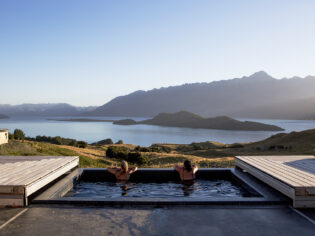 Two people relax in a tranquil pool, taking in the breathtaking alpine scenery surrounding Aro Ha Wellness Retreat.