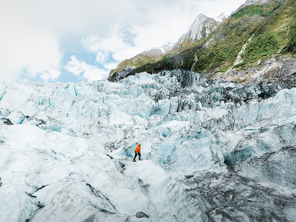 A lone hiker trekking across icy glacier terrain.