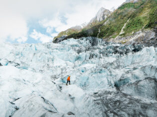 A lone hiker trekking across icy glacier terrain.