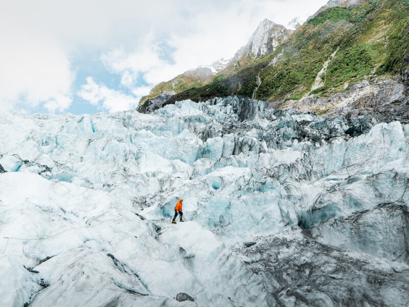 A lone hiker trekking across icy glacier terrain.