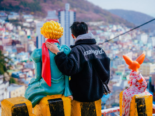 a man sitting beside The Little Prince statue in Busan overlooking Gamcheon Culture Village
