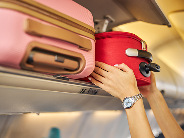 A woman lifting her carry-on bag into the overhead compartment of a plane