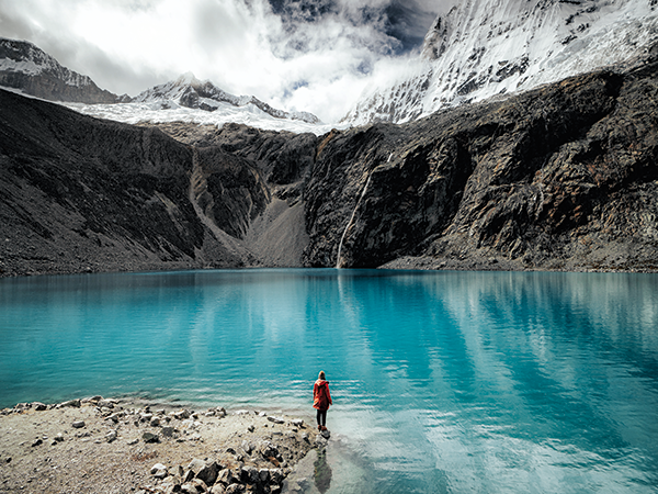 Person standing by the turquoise waters of Laguna 69 with glacier views in the Peru Highlands.