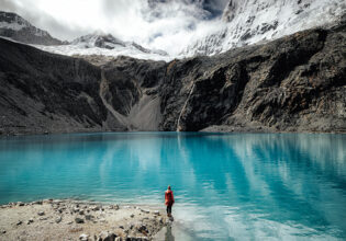 Person standing by the turquoise waters of Laguna 69 with glacier views.