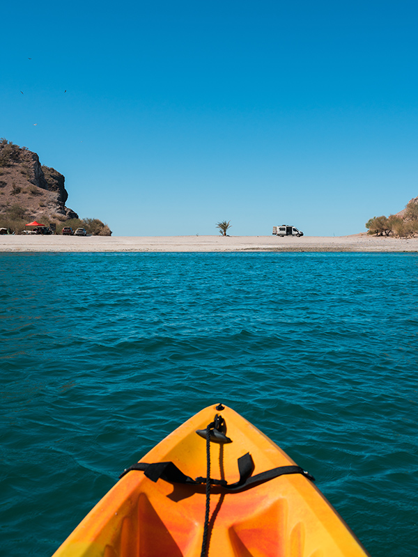 A POV from a kayak gliding over calm waters, with the vast blue sea ahead and an endless sky above.