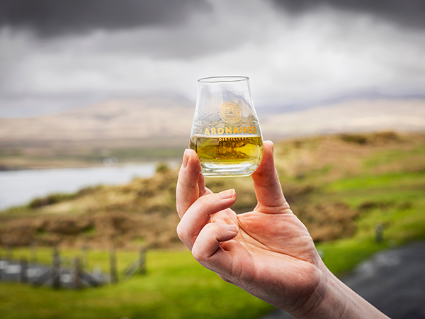 A person holding a glass of whisky against sweeping views of Scotland in Northern Europe and the UK.