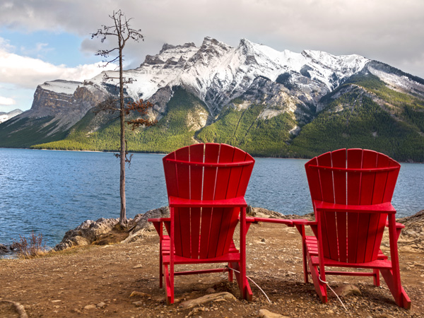 Red Adirondack chairs overlooking Lake Minnewanka in Canada