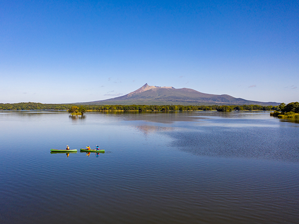 Kayakers paddle across a serene lake surrounded by towering mountains in Hokkaido Prefecture, showcasing the region’s breathtaking natural beauty.