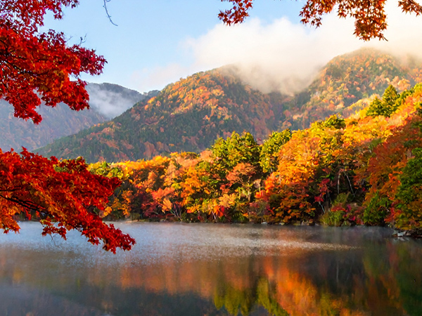 A serene river in Japan flows beneath mountains painted in autumn hues — the perfect place to get beautifully lost.