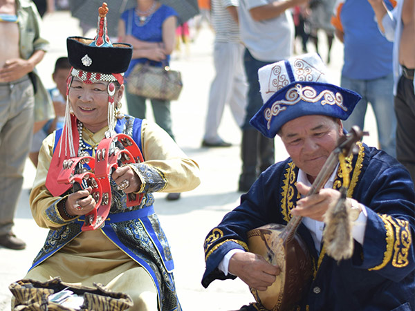 man in blue and white long sleeve shirt wearing red hat playing guitar at naadam festival