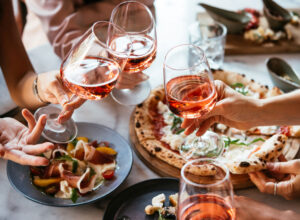 Friends enjoy a dinner party with pizza and rose wine in a bar or a restaurant.
