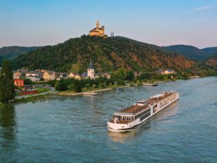 Viking River Cruise ship, the Mimir, passing the historic Marksburg Castle near Braubach on the Rhine River at sunset.