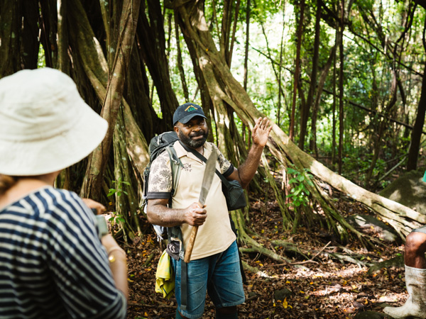 A local guide talks to the hiking group near a fig tree
