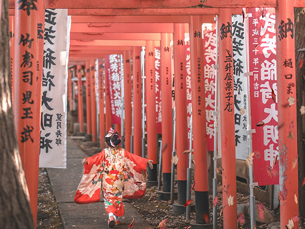 little girl in geisha outfit funning through red arches in japan