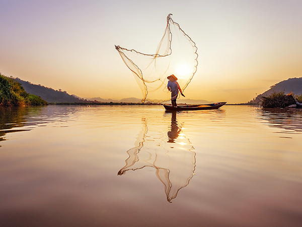 A fisherman casts his net into the Mekong River.