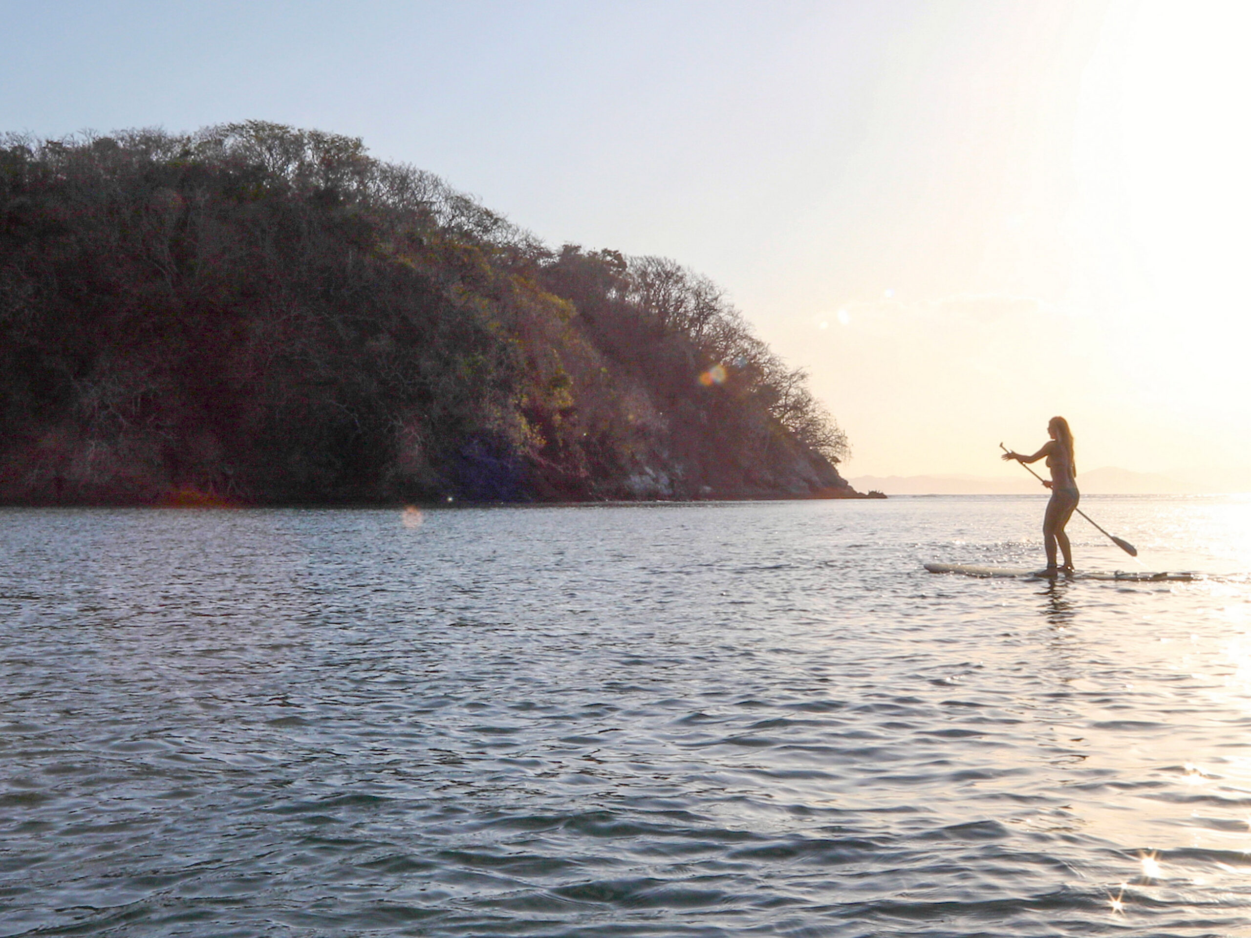 Young woman paddle boards in the Pacific Ocean near panama at sunrise